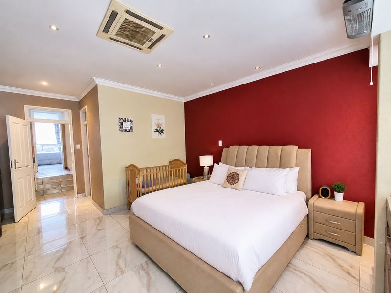 Spacious bedroom featuring tiled flooring, recessed ceiling lighting, and a ducted air conditioning unit, with a bold red accent wall.