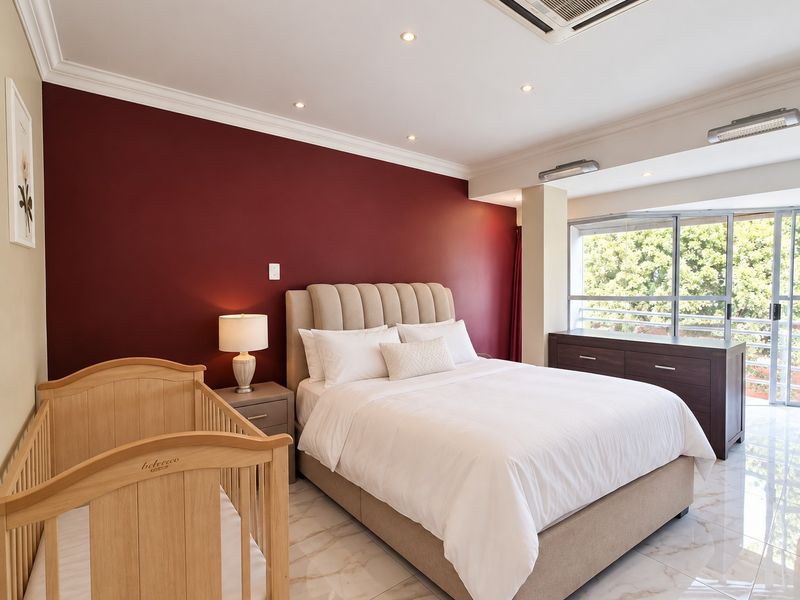 Spacious bedroom featuring marble-look tiled flooring, recessed ceiling lighting, integrated ducted air conditioning, and large sliding glass doors leading to a balcony.