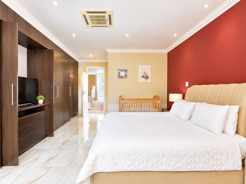 Spacious bedroom featuring marble-look tiled flooring, extensive built-in cabinetry, recessed lighting, ducted air conditioning, and direct access to an en-suite bathroom.