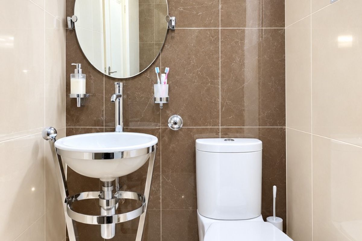A modern, compact guest bathroom featuring high-gloss ceramic wall tiles, a contemporary wall-mounted basin with chrome stand, and a sleek dual-flush toilet.