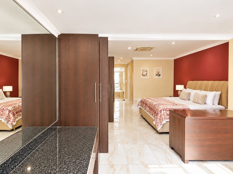 Spacious bedroom featuring built-in cupboards, a granite vanity area, polished tiled flooring, and integrated ducted air conditioning.