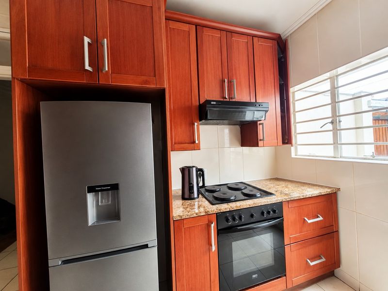 A functional kitchen featuring warm-toned wooden cabinetry, granite countertops, a built-in oven, electric hob, and an extractor fan.