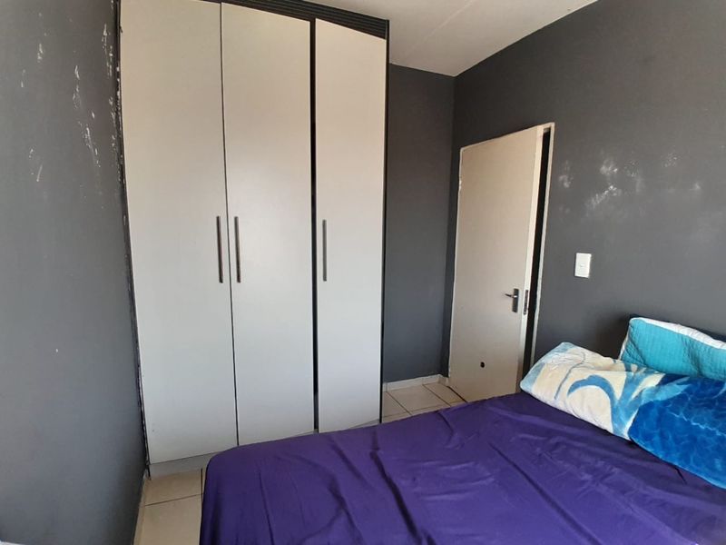 A bedroom featuring a built-in wardrobe and tiled flooring, currently requiring cosmetic updates to the wall finishes and door.
