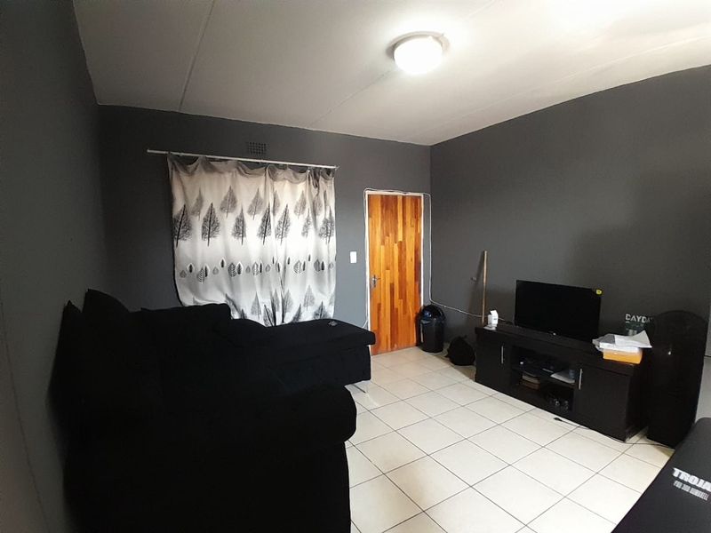 A living room featuring tiled flooring, dark grey walls, and a wooden door, providing a functional space for relaxation.