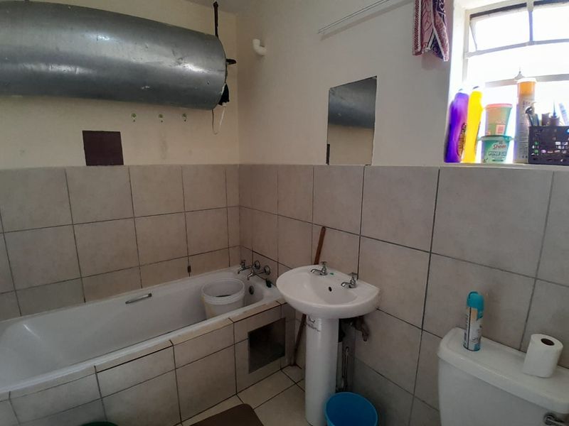 A functional bathroom featuring a bathtub, pedestal basin, and toilet with tiled finishes. The space requires cosmetic updates and modernization of fixtures.