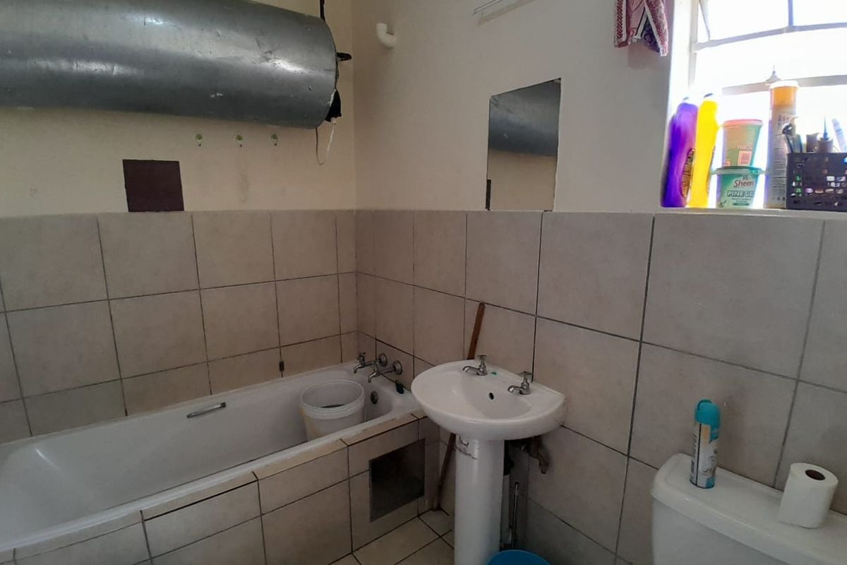 A functional bathroom featuring a bathtub, pedestal basin, and toilet with tiled finishes. The space requires cosmetic updates and modernization of fixtures.