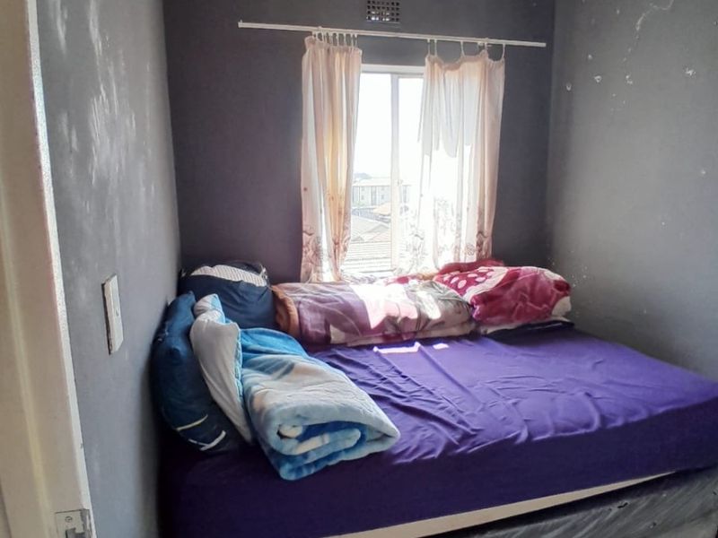 A compact bedroom featuring tiled flooring and dark-painted walls that show signs of wear and require maintenance.