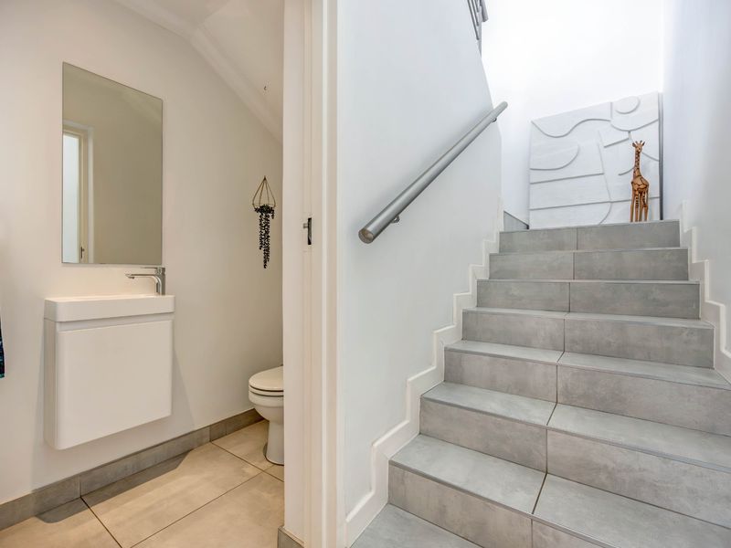 A bright hallway featuring a modern staircase with a metal handrail, adjacent to a compact guest bathroom with a wall-mounted vanity and toilet.