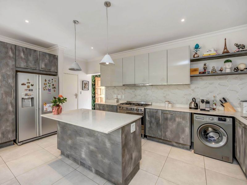 Modern kitchen featuring a central island, stone countertops, gas stove, hexagonal tile backsplash, and ample built-in cabinetry with a contemporary finish.