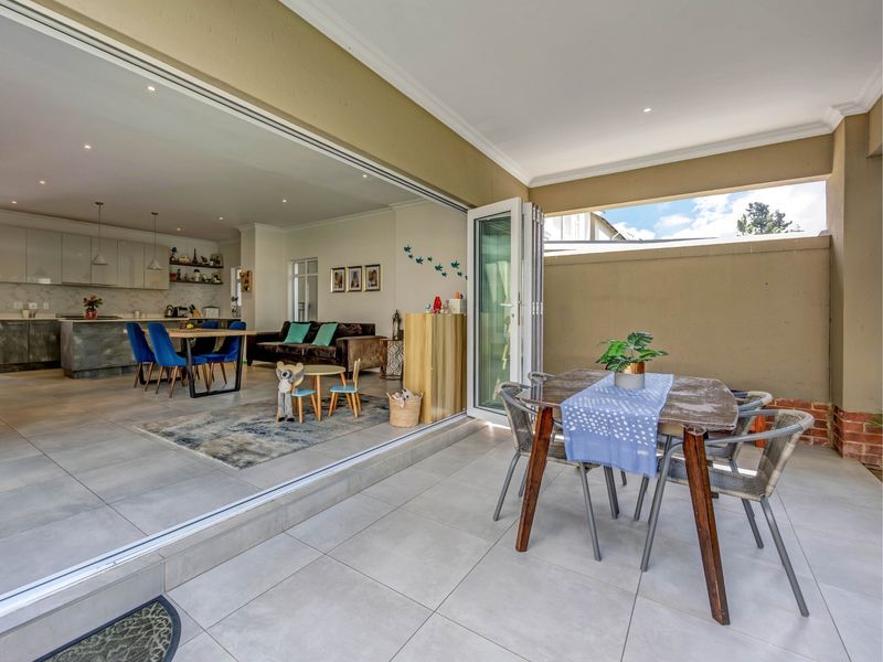 Spacious open-plan living area seamlessly connecting to a covered patio through large bi-fold doors, featuring modern kitchen finishes and neutral tiled flooring.