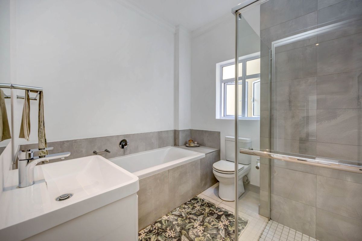 Modern bathroom featuring a built-in bathtub, glass-enclosed shower, vanity basin, and toilet with neutral grey tiling.