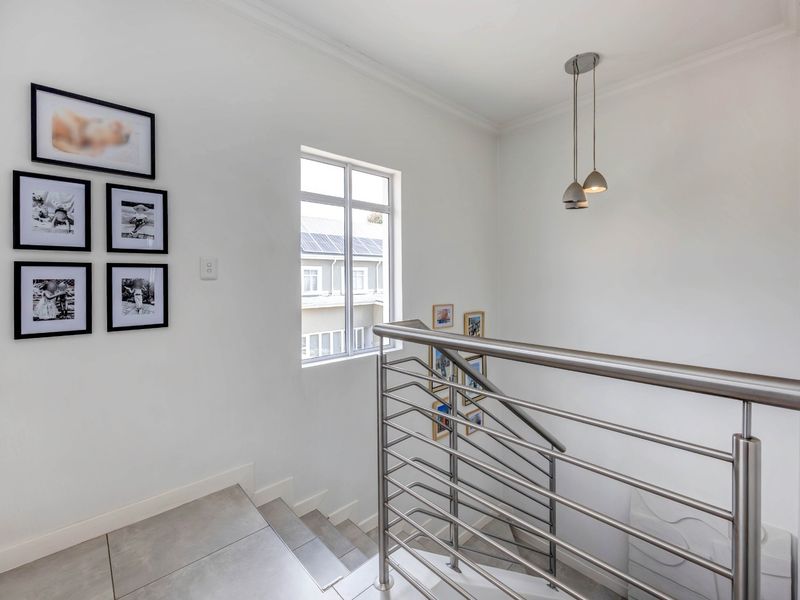 A bright, modern staircase landing featuring a sleek stainless steel balustrade, tiled flooring, and contemporary pendant lighting.