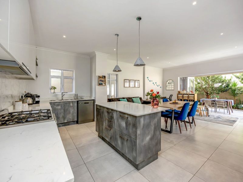 Modern open-plan kitchen and living area featuring a central island, stone countertops, gas hob, and seamless flow to the outdoor patio through sliding doors.