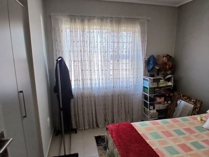 A functional bedroom featuring tiled flooring, a built-in wardrobe, and a window with curtain treatments, providing a neutral base for interior design.