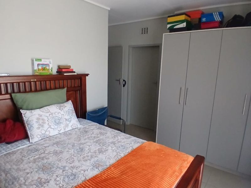 A functional bedroom featuring neutral wall tones, tiled flooring, and a built-in wardrobe providing ample storage space.