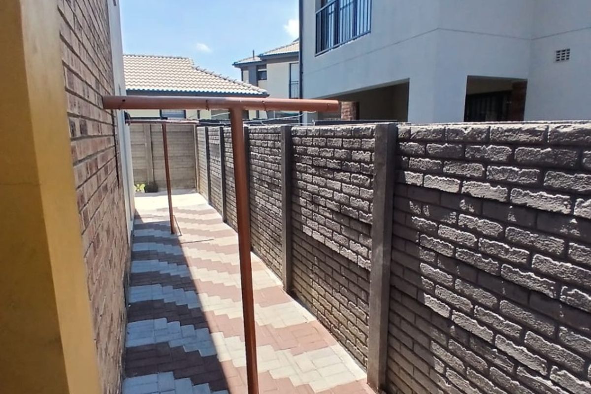 A side passage featuring a paved walkway, brick boundary walling, and a fixed metal washing line structure.