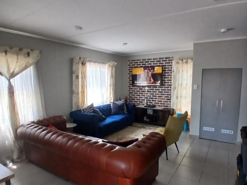 A living room featuring a brick accent wall, tiled flooring, and a built-in storage cupboard.