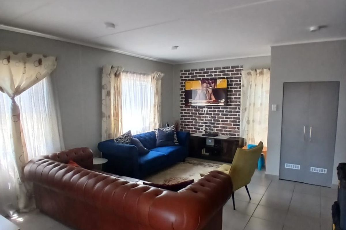 A living room featuring a brick accent wall, tiled flooring, and a built-in storage cupboard.