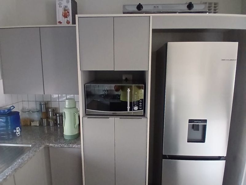 A functional kitchen featuring modern grey cabinetry, granite countertops, a built-in microwave, and tiled flooring with a clean, contemporary aesthetic.