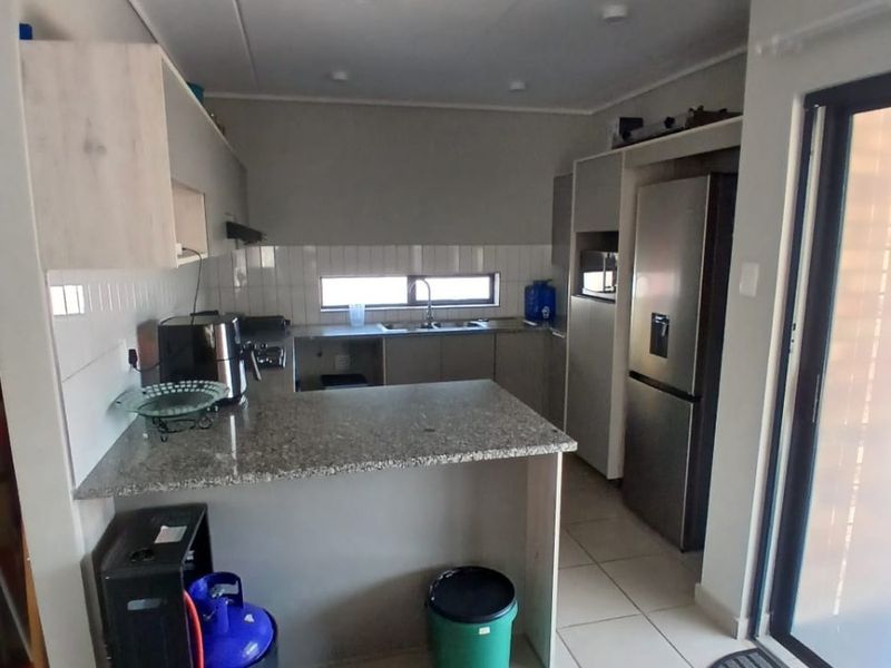 Modern kitchen featuring granite countertops, tiled backsplash, ample built-in cabinetry, and tiled flooring with direct access to an outdoor area.