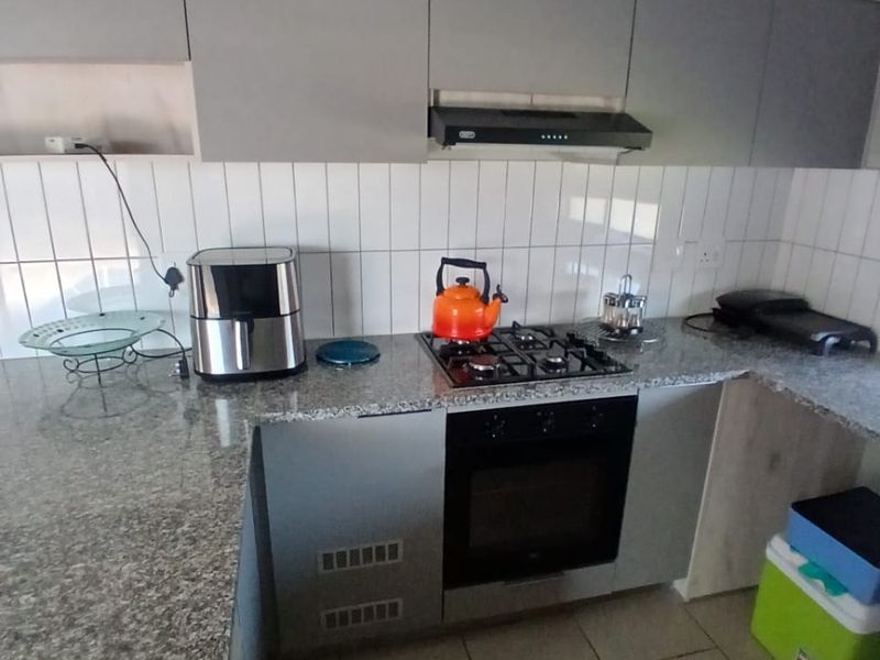 A functional kitchen featuring granite countertops, built-in oven, gas hob, extractor fan, and modern grey cabinetry with a clean tiled backsplash.
