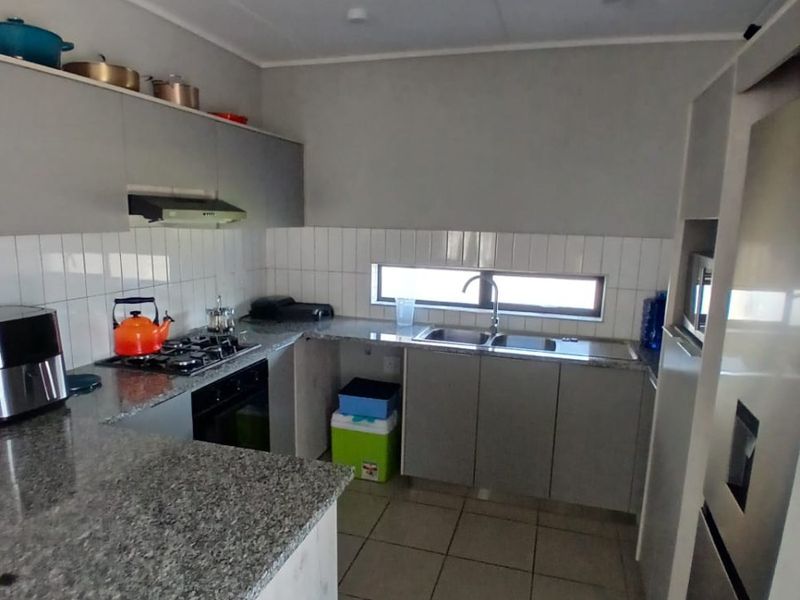 A functional kitchen featuring granite countertops, built-in cabinetry, a gas hob with extractor fan, and a double basin sink with tiled backsplash.