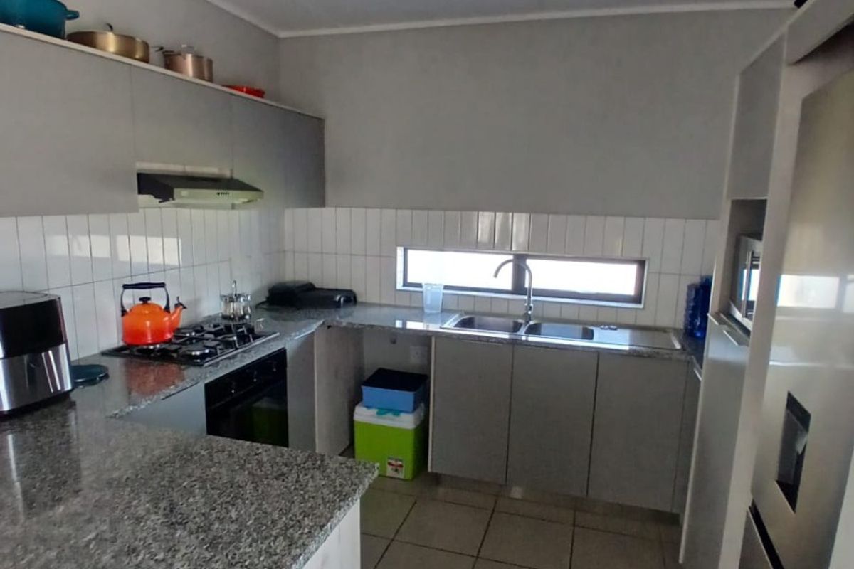 A functional kitchen featuring granite countertops, built-in cabinetry, a gas hob with extractor fan, and a double basin sink with tiled backsplash.