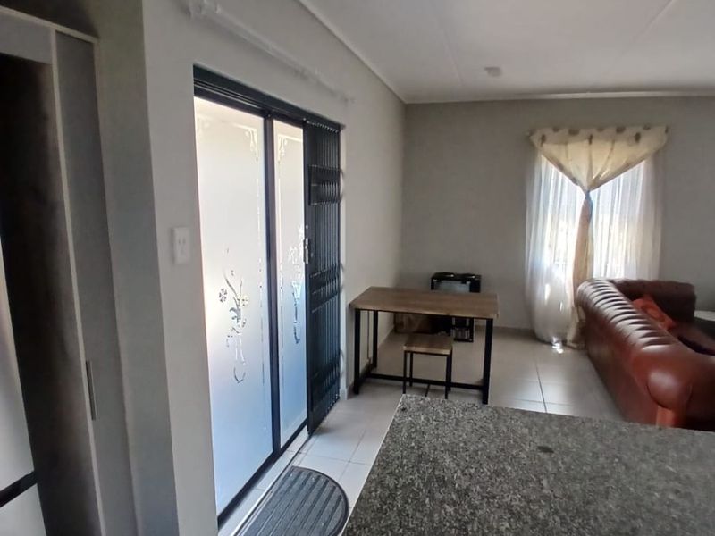 Open plan living area featuring tiled flooring, a granite kitchen countertop, and a sliding glass door with security gate leading to the exterior.