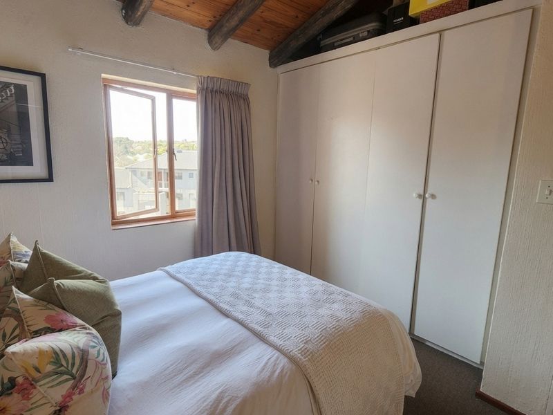 A cozy bedroom featuring exposed timber ceiling beams, a built-in wardrobe, and a casement window providing natural light.
