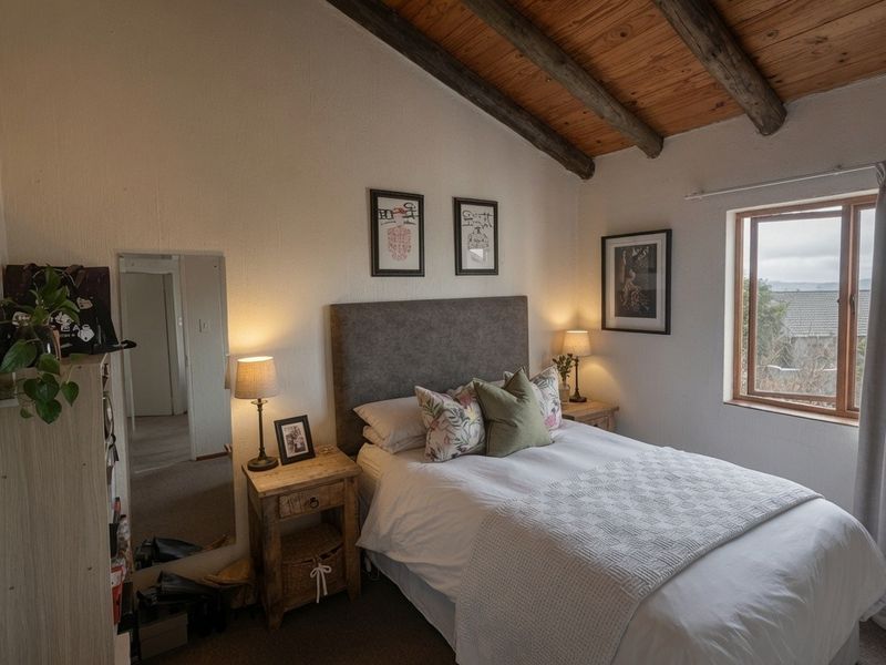 A cozy bedroom featuring a sloped ceiling with exposed timber beams and a window providing natural light.