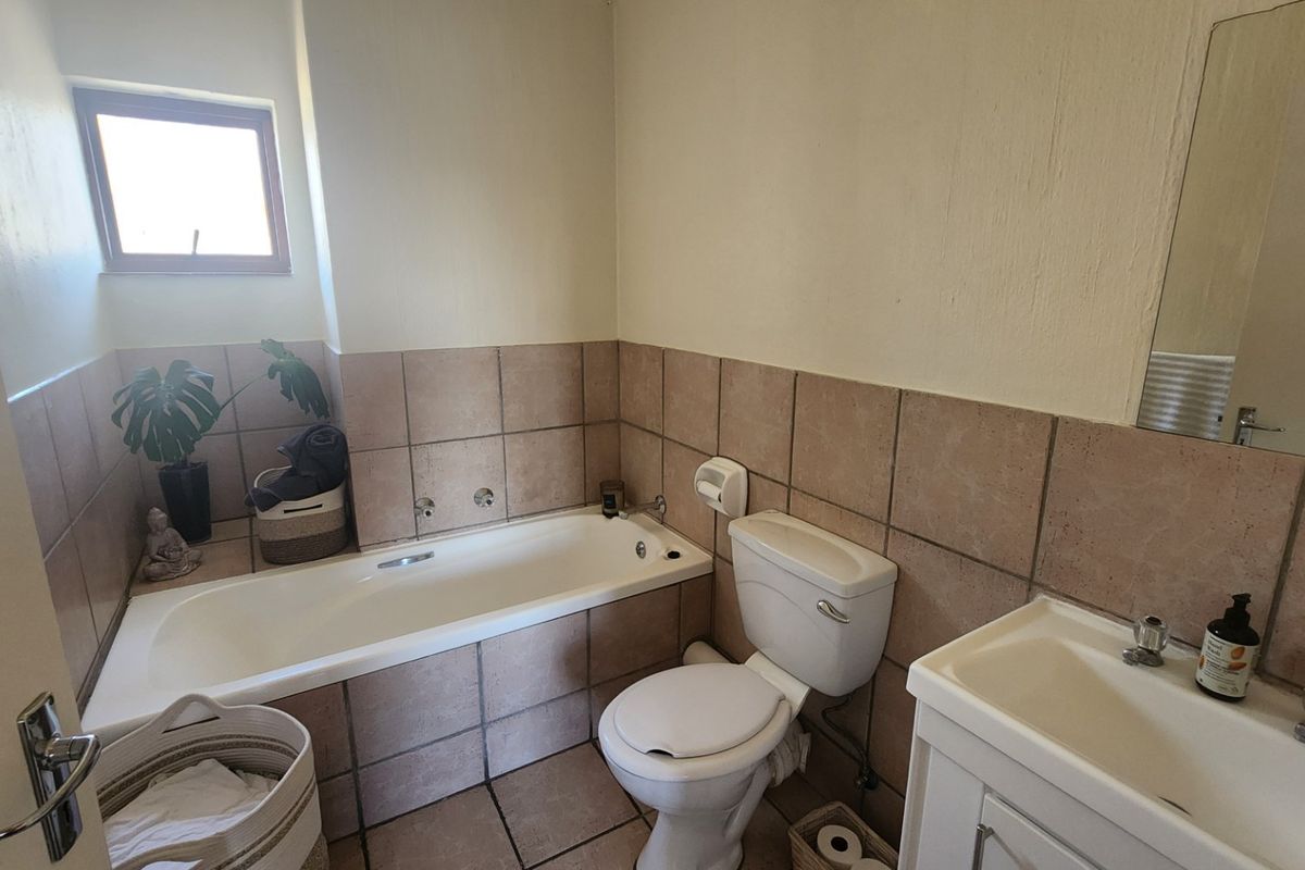 A functional bathroom featuring a bathtub, toilet, and vanity basin with tiled finishes, offering a practical layout with potential for cosmetic updates.