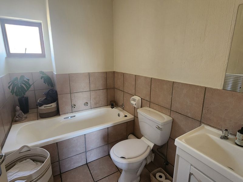 A functional bathroom featuring a bathtub, toilet, and vanity basin with tiled finishes, offering a practical layout with potential for cosmetic updates.