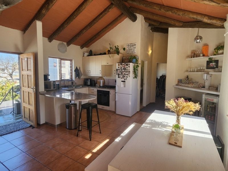 Open-plan kitchen and living area featuring exposed timber ceiling beams, tiled flooring, and a functional kitchen layout with granite countertops.