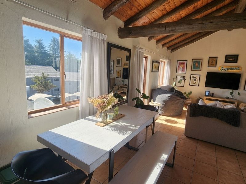 Open-plan living and dining area featuring exposed timber ceiling beams, tiled flooring, and large windows providing natural light.