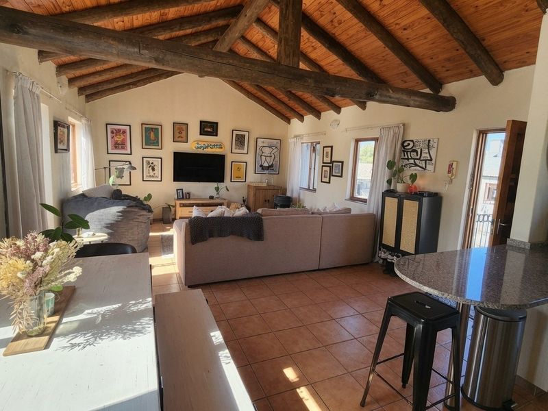 Spacious open-plan living and kitchen area featuring high vaulted ceilings with exposed timber beams and durable terracotta floor tiles.