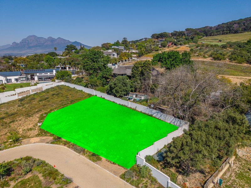 Aerial view of a vacant residential plot featuring a perimeter wall and paved access road in a scenic neighborhood setting.