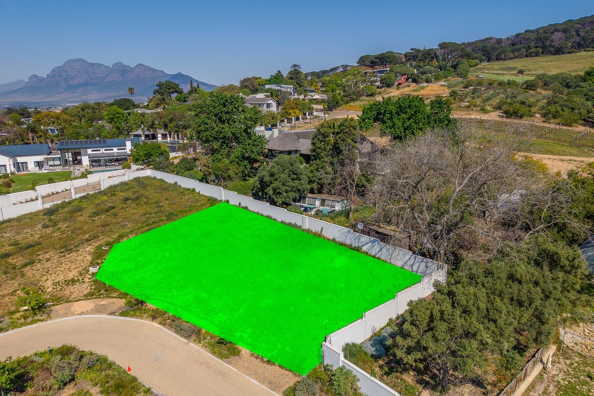 Aerial view of a vacant residential plot featuring a perimeter wall and paved access road in a scenic neighborhood setting.