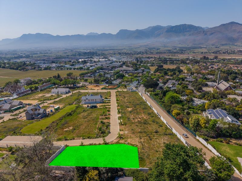 Aerial view of a vacant residential plot in a developed estate, featuring paved road access and mountain views.