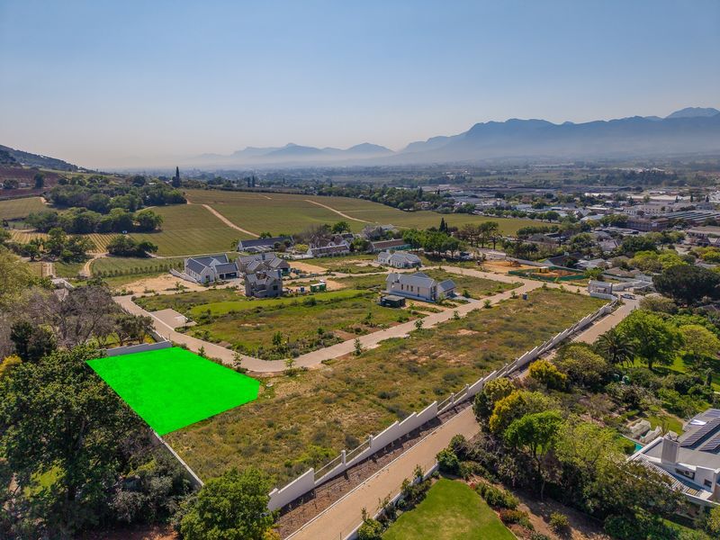Aerial view of a vacant residential plot in a developed estate, featuring clear boundary demarcations and surrounding mountain and vineyard views.