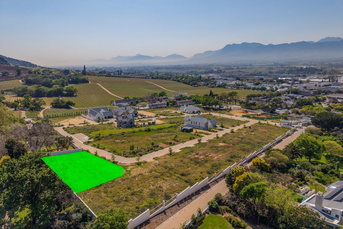Aerial view of a vacant residential plot in a developed estate, featuring clear boundary demarcations and surrounding mountain and vineyard views.