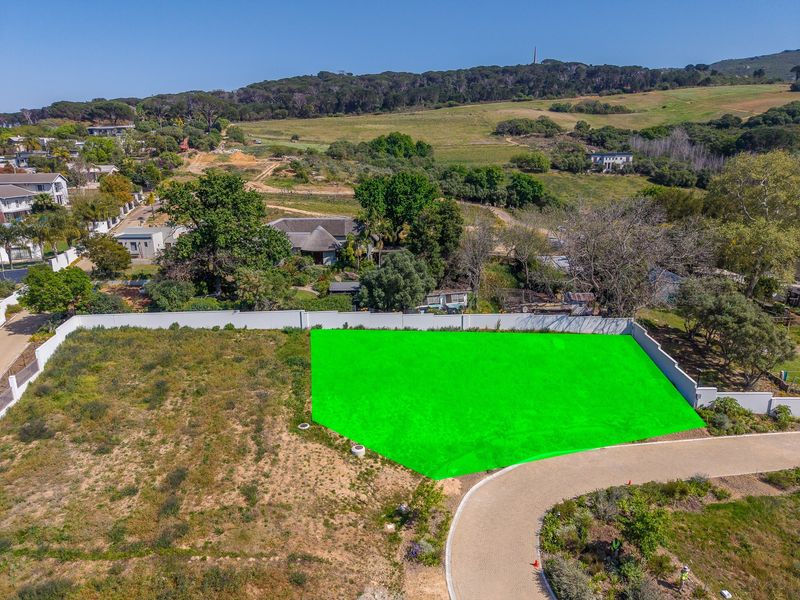 Aerial view of a vacant residential plot featuring a boundary wall and paved driveway access in a scenic estate setting.