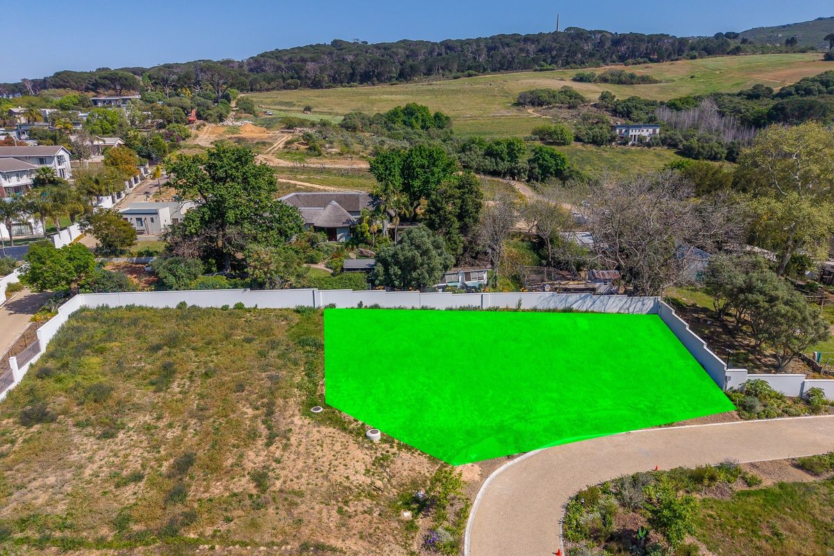 Aerial view of a vacant residential plot featuring a boundary wall and paved driveway access in a scenic estate setting.