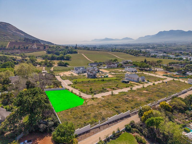 Aerial view of a vacant residential plot highlighted in green, situated within a developed estate with mountain views and established infrastructure.