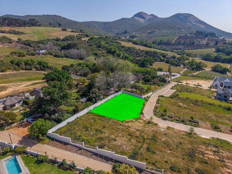Aerial view of a vacant residential plot featuring boundary walls and access road, set within a scenic landscape with mountain views.