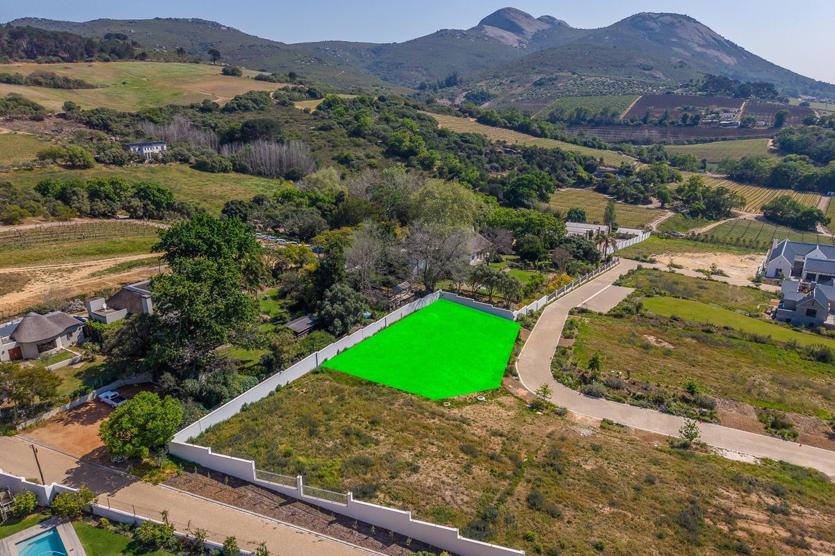 Aerial view of a vacant residential plot featuring boundary walls and access road, set within a scenic landscape with mountain views.
