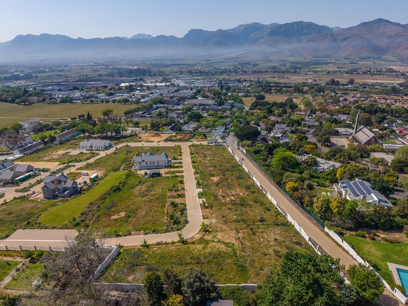 Aerial view of a residential development site featuring paved access roads, boundary walls, and surrounding mountain landscape.