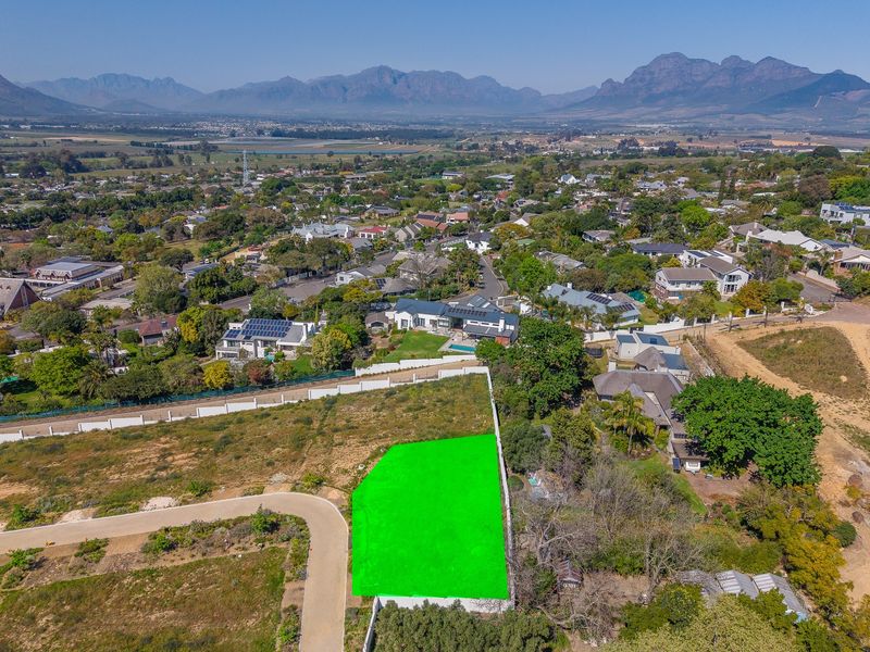 Aerial view of a vacant residential plot with boundary walls and access road, situated in a scenic estate with mountain views.