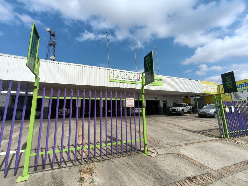 Front exterior view of a commercial automotive workshop featuring a concrete driveway, steel palisade fencing, and prominent business signage.