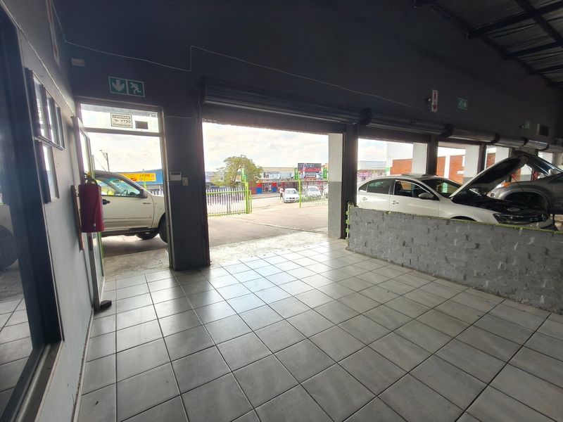 Spacious commercial garage area featuring tiled flooring, roller shutter doors, and essential safety fixtures, suitable for automotive or workshop use.
