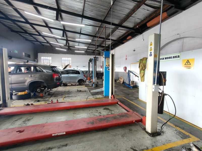 A functional automotive workshop featuring multiple vehicle lifts, exposed industrial ceiling, and concrete flooring, currently set up for vehicle maintenance and repairs.